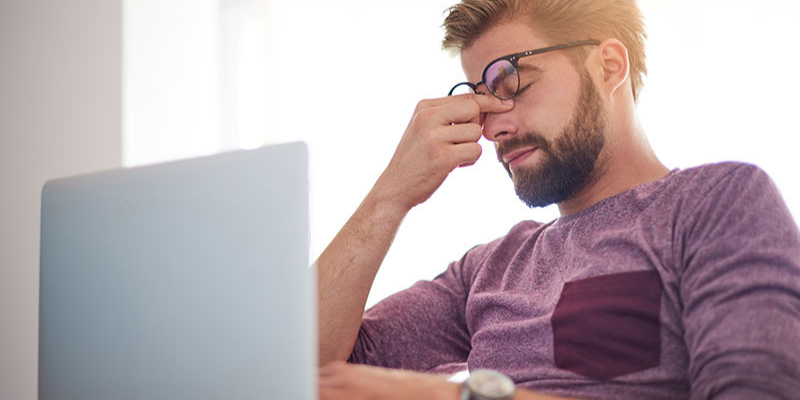 Person pinching bridge of nose looking at computer screen