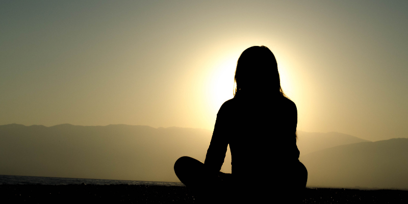 Silhouette of a person sitting in front of a sunset