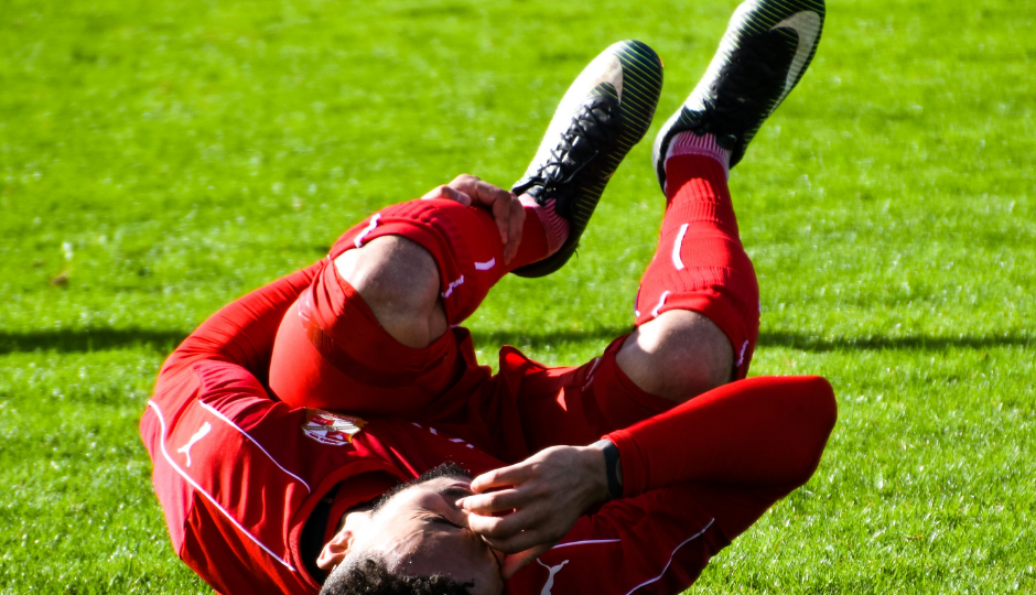 Soccer player laying on ground and holding shin