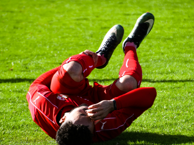 Soccer player laying on ground and holding shin