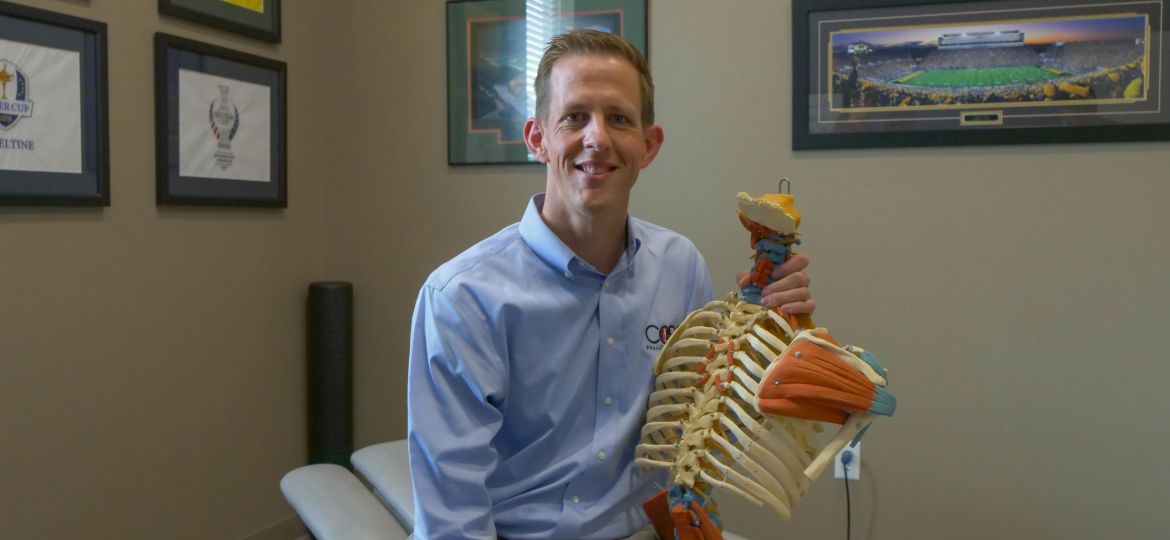 man sitting on physical therapy bench holding skeleton